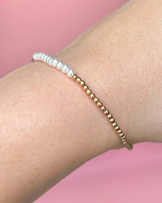 Bracelet with white beads and gold beads on a wrist against a pink background