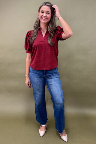 Woman wearing a red blouse and blue jeans against a green background