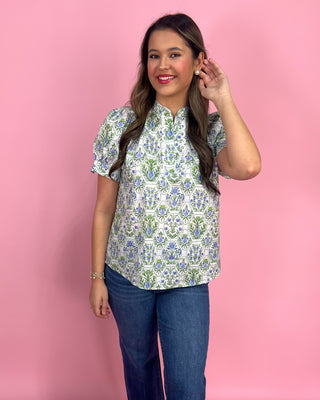 Woman wearing a floral blouse and jeans against a pink background