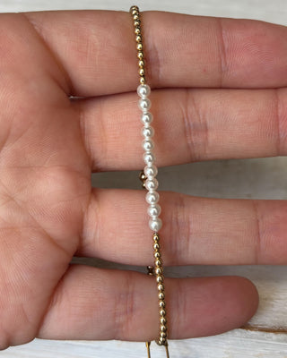 Gold and pearl bracelet on a hand against a neutral background