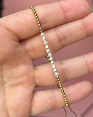 Gold and pearl beaded bracelet on a hand with a blurred background