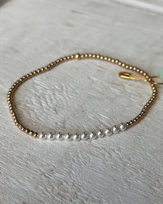 Gold bracelet with small pearls on a light wooden surface