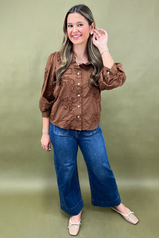 Woman wearing a brown blouse and blue jeans against a green background