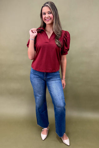 Woman wearing a red blouse and blue jeans against a green background