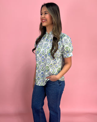 Woman wearing a floral blouse and jeans against a pink background