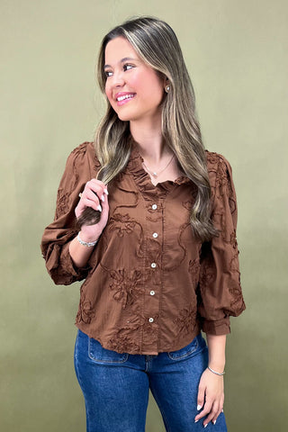 Woman wearing a brown blouse with floral details against a green background