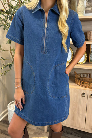 Woman wearing a blue denim dress with a zipper in a home setting.