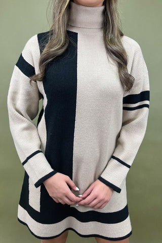 Person wearing a beige and black ribbed sweater dress against a green background