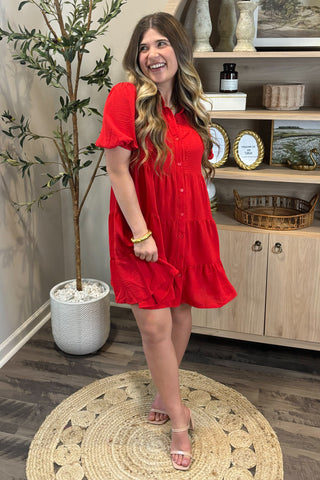 Woman in a red dress standing in a room with a plant and wooden cabinet.