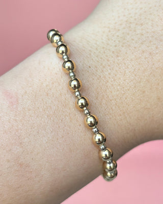 Gold beaded bracelet on a wrist with a pink background