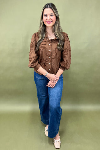 Woman wearing a brown blouse and blue jeans against a green background