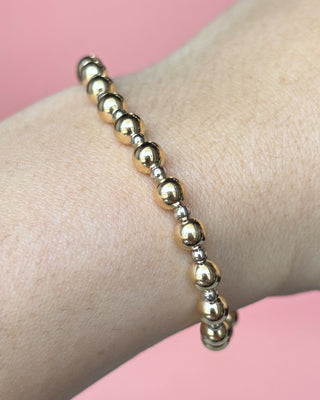 Gold beaded bracelet on a wrist with a pink background