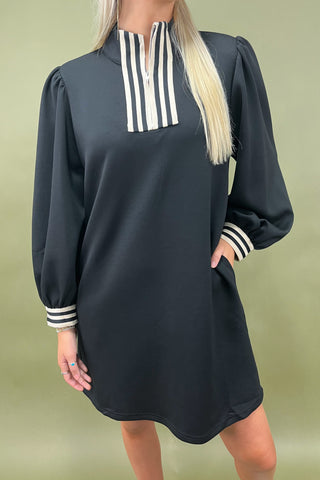 Black dress with white striped accents worn by a person on a green background