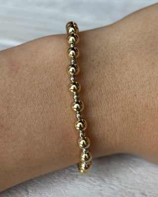 Gold beaded bracelet on a wrist against a white background