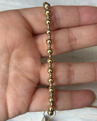 Gold beaded bracelet held between fingers against a neutral background