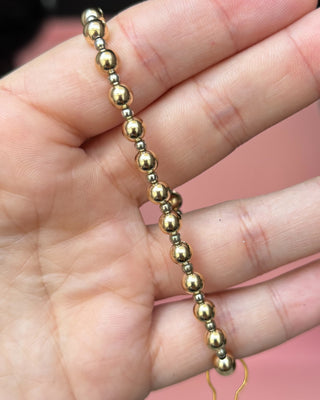 Gold beaded necklace on a hand with a pink background