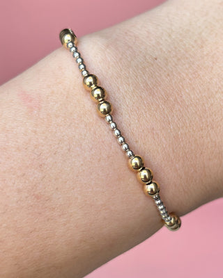 Gold and silver beaded bracelet on a wrist with a pink background