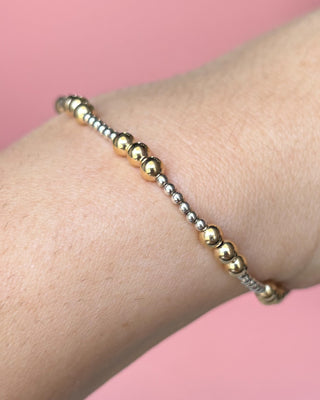 Gold beaded bracelet on a wrist with a pink background