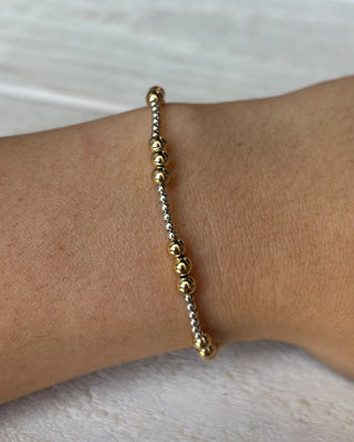 Gold beaded bracelet on a wrist against a white background