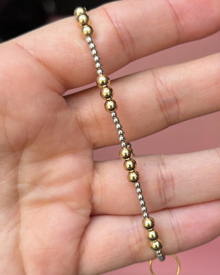Gold and silver beaded bracelet on a hand with a pink background