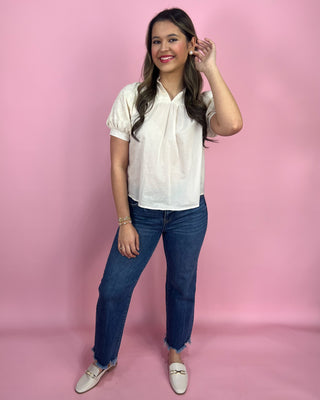 Woman wearing a white blouse and blue jeans against a pink background