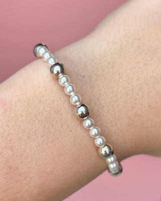Pearl and black bead bracelet on a wrist against a pink background
