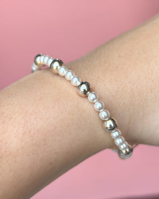 Pearl and silver beaded bracelet on a wrist against a pink background