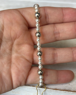 Hand holding a bracelet with alternating pearls and metallic beads on a neutral background