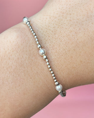 Pearl bracelet on a wrist against a pink background