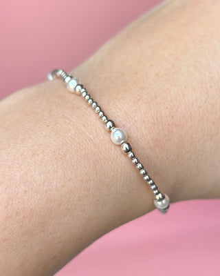 Silver beaded bracelet on a wrist with a pink background
