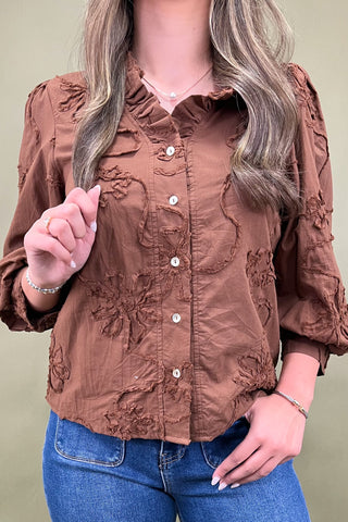 Brown textured blouse with ruffled details worn by a person against a beige background