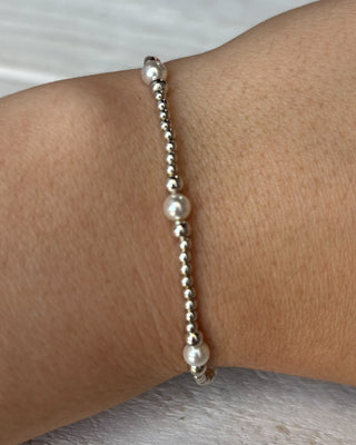 Silver beaded bracelet with a pearl on a wrist against a neutral background