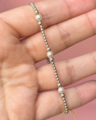 Bracelet with alternating silver beads and pearls on a hand against a pink background