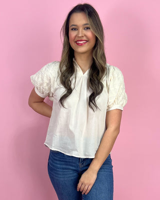 Woman wearing a white blouse with lace sleeves against a pink background