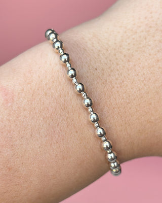 Silver beaded bracelet on a wrist with a pink background