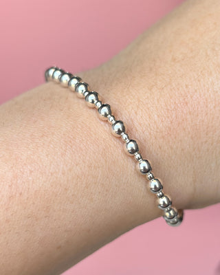 Silver beaded bracelet on a wrist with a pink background