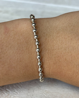 Silver beaded bracelet on a wrist with a neutral background