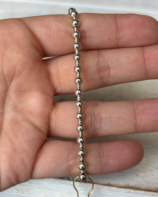 Silver beaded chain held between fingers on a neutral background