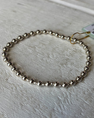 Silver beaded bracelet on a light wooden surface with a tag attached.
