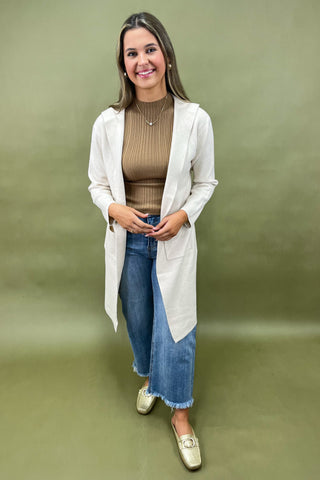 Beige longline cardigan layered over ribbed camel top styled with light wash wide leg jeans and gold loafers