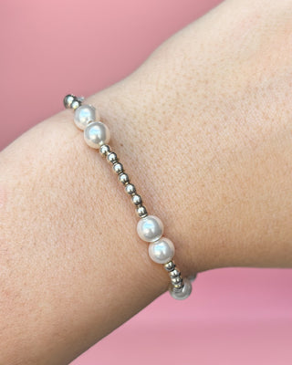 Pearl bracelet on a wrist with a pink background