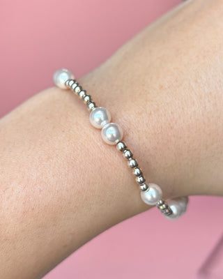 Pearl bracelet on a wrist with a pink background