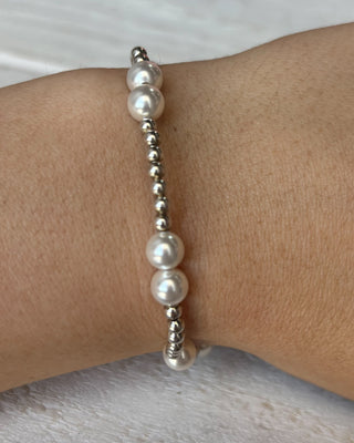 Pearl and silver beaded bracelet on a wrist against a neutral background