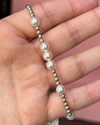 Pearl and silver bead bracelet on a hand against a pink background
