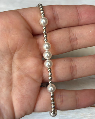 Bracelet with alternating silver and pearl beads held in a hand against a neutral background
