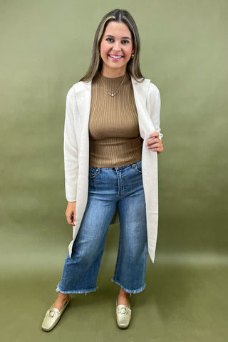 Beige longline cardigan layered over ribbed camel top styled with light wash wide leg jeans and gold loafers