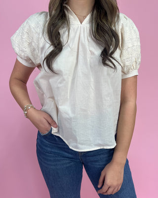 Person wearing a white blouse with short sleeves and blue jeans against a pink background