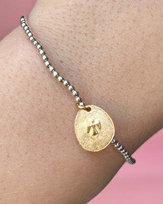 Bracelet with a gold coin charm on a wrist against a pink background