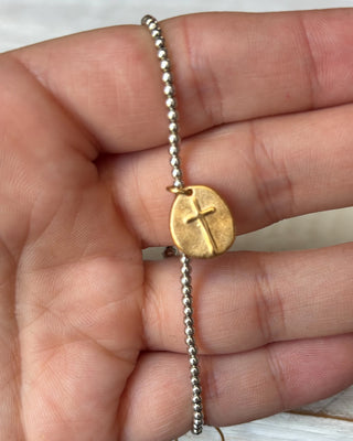 Gold bracelet with a cross charm held in a hand against a neutral background