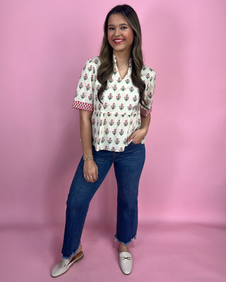 Woman wearing a floral blouse and blue jeans against a pink background